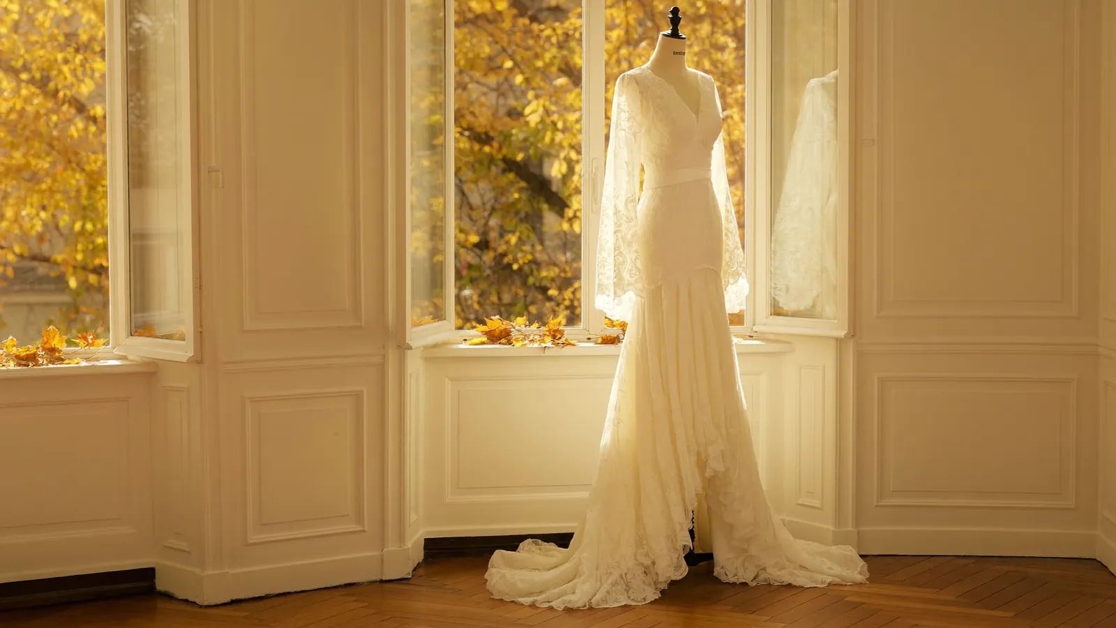 Brautkleid mit langen Spitzenärmeln an einer Schneiderpuppe, warmes Herbstlicht fällt durch ein hohes Atelierfenster